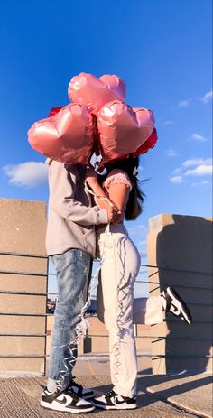 a man and woman standing next to each other with pink balloons on their heads,