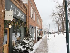 a snowy street lined with shops and trees on the side of it's sidewalk