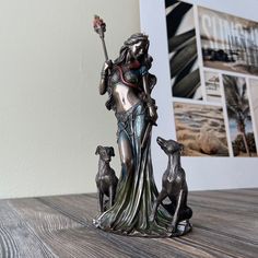 a statue of a woman holding a staff with two dogs on the table next to it