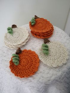 four crocheted pumpkin coasters sitting on top of a white cloth covered table