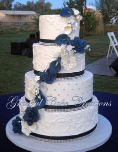 a three tiered wedding cake with blue and white flowers on the top, sitting on a table outside