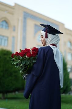 a woman wearing a graduation gown and holding a bouquet of roses in front of a building