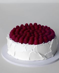 a white cake topped with fresh raspberries on top of a white platter