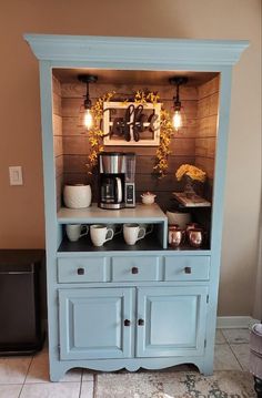 a blue hutch with coffee maker and cups on it's side, sitting in front of a brown wall