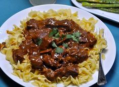 a white plate topped with pasta covered in meat and sauce next to asparagus