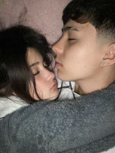 a man and woman kissing each other while laying on a bed with their eyes closed