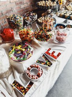 a table topped with lots of different types of candies and desserts next to a brick wall