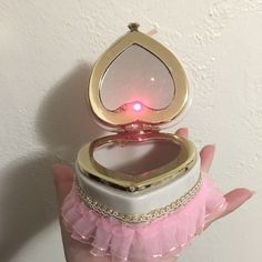 a hand holding a small white and gold ring case with pink tulle skirt on it