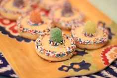 some cookies with sprinkles are on a colorful plate and there is a small green gummy bear in the middle