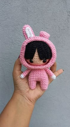 a hand holding a small crocheted doll wearing a pink bunny outfit with ears