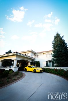 a yellow sports car is parked in front of a large white house with trees and bushes