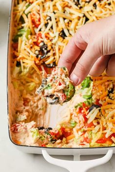 a hand dipping a tortilla chip into a casserole dish with cheese and black olives