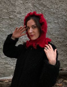 a woman wearing a black coat and red scarf with her hand up to her face