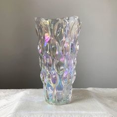 a clear glass vase sitting on top of a white tablecloth covered table with a gray wall in the background