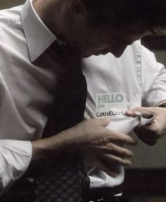 a man in white shirt and black tie using his cell phone while sitting at a desk