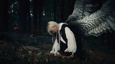 a woman kneeling down next to an owl in the woods with wings spread wide open