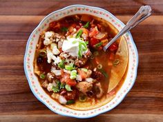 a bowl of soup with meat, vegetables and sour cream in it on a wooden table