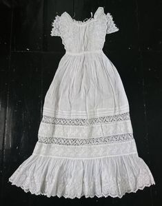 A beautifully decorative little Christening gown dating to the 19th century. Light weight cotton, the bodice is vertically pleated front and back, fastening with ties. At the front are bands of crochet lace on each side, with flounces of floral embroidered whitework running up and around the neck. Under the flounce are short sleeves, embroidered tulle lace with a scalloped edge. The skirt is pleated in to the waist, opening out to a narrow bell shape with alternating bands of pleats, lace and em Victorian Cotton Dress With Historical Design, White Cotton Prairie Dress For Wedding, White Historical Dress For Daywear, Victorian Cotton Daywear Dress, Vintage Cotton Dress With Historical Design, Cotton Dress With Historical Design For Wedding, Victorian Cotton Dress With Broderie Anglaise, White Cotton Victorian Dress For Wedding, White Cotton Victorian Wedding Dress