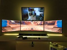 three computer monitors sitting on top of a desk next to each other in front of a flat screen tv