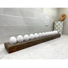 eight eggs are lined up in a row on a wooden stand next to a tile wall