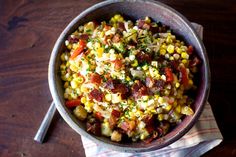 a bowl filled with corn and bacon on top of a napkin next to a spoon