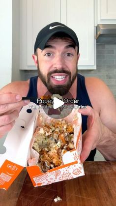 a man holding up a box of food on top of a wooden table in front of him