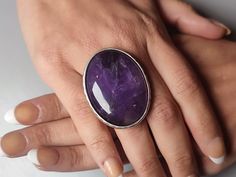 Crafted with precision and care, this handmade adjustable amethyst ring is a captivating piece of womens jewellery that captures the essence of elegance and individuality. The striking oval amethyst, the February birthstone, takes centre stage in this adjustable ring, its deep purple hue symbolising tranquillity and inner strength. The large, bold setting of this ring makes it an unusual and eye-catching choice, perfect for those who seek to make a statement with their accessories. Whether worn Oval Crystal Ring For Jewelry Making, Handmade Adjustable Oval Crystal Ring, Amethyst Rings With Large Oval Stone, Adjustable Crystal Ring With Large Stone, Adjustable Oval Purple Amethyst Ring, Adjustable Amethyst Ring With Natural Stones, Adjustable Oval Cabochon Crystal Ring Gift, Oval Amethyst Ring With Large Stone, Adjustable Oval Cabochon Ring With Large Stone