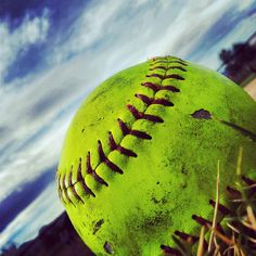 a green baseball sitting on top of grass next to a blue sky with clouds in the background