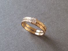 two gold wedding rings sitting on top of a gray surface with a diamond in the middle