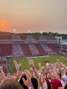 a football stadium filled with lots of people holding their hands up in the air as the sun sets