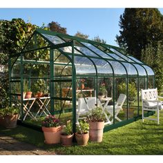 a small green house sitting on top of a lush green field next to a white lawn chair