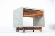 a concrete and wood side table sitting on top of a white floor next to a wall