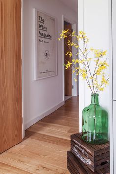 a green vase with yellow flowers in it sitting on a wooden crate next to a door