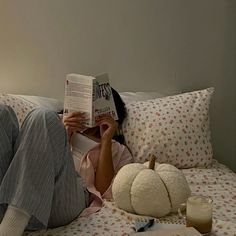 a woman laying in bed reading a book and holding a pumpkin next to her face