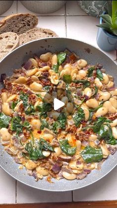 a pan filled with pasta and spinach on top of a table next to bread