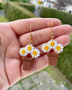 a hand holding a pair of earrings with daisies on them in front of a house