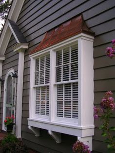 a gray house with white shutters and pink flowers