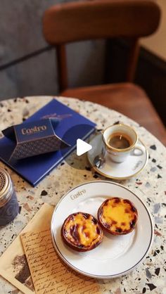 two pastries on a white plate next to a cup of coffee and a book