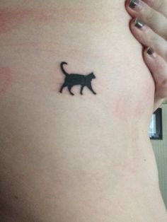 a small black cat tattoo on the side of a woman's stomach is shown