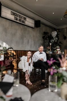 a man and woman sitting on chairs in a room filled with tables, flowers and balloons