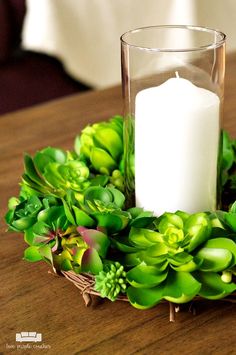 a candle and some green plants are on a table with a white candle in the middle