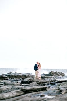 a man and woman standing on rocks near the ocean