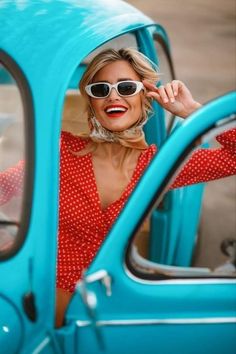 a woman wearing sunglasses sitting in the driver's seat of a blue car smiling