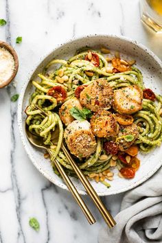 a white bowl filled with pasta and scallops on top of a marble table