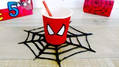 a red cup sitting on top of a table next to a spider web net with a straw in it