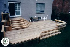 a wooden deck in front of a house with chairs on the side and steps leading up to it