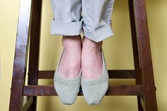 a woman sitting on top of a wooden step stool wearing gray slippers and grey pants