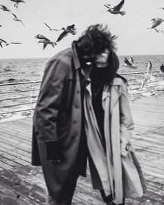 a man standing on a pier with birds flying over him and the ocean in the background