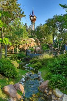 a small stream running through a lush green forest next to a tall tower in the distance