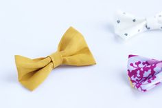 three small bow ties sitting next to each other on a white surface, one yellow and the other pink